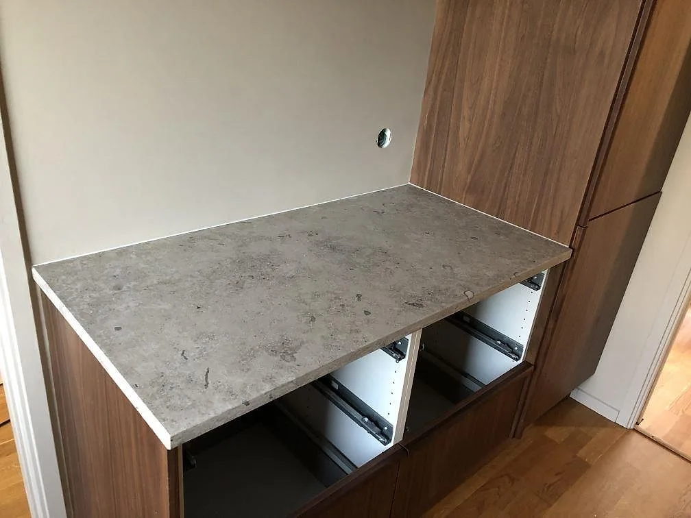 Fristående bänkskiva i 30 mm Jura Grey kalksten, matt, monterad på en valnötsfärgad köksrad i ett kök i Torekov.