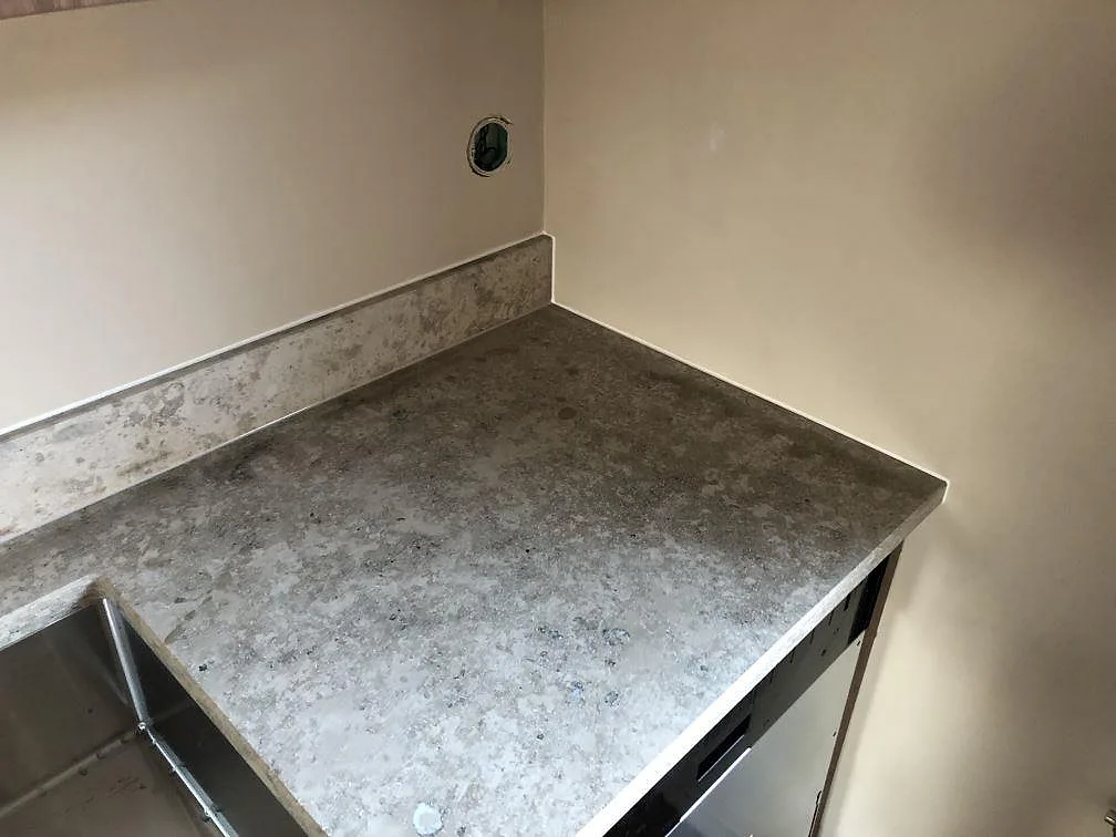 Matt köksbänkskiva i Jura Grey kalksten i en köksvrå med uppvikt stänkskydd på två väggar i ett kök i Torekov.