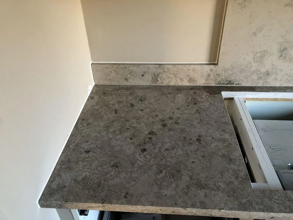 Hörnparti av en matt köksbänkskiva i Jura Grey kalksten med fossila spår och uppvikt stänkskydd på mörka köksstommar i ett kök i Torekov.