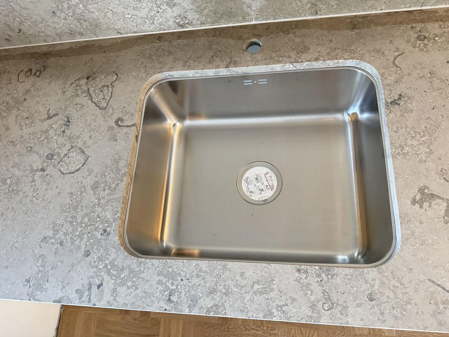 Närbild av rostfri diskho monterad i matt Jura Grey kalksten med synliga fossilteckningar i Västra Frölunda.