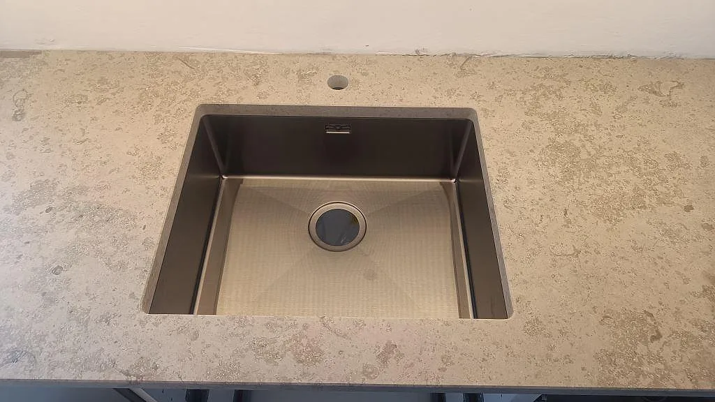 Närbild på underlimmad rostfri diskho i en köksbänkskiva av matt Jura Grey kalksten i Varberg.
