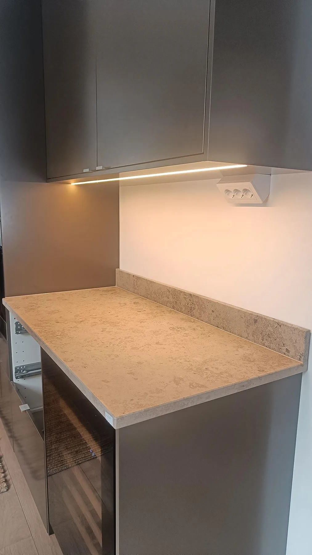 Installerad köksbänkskiva i matt Jura Grey kalksten med uppvikt stänkkant och mörka skåp i Varberg.