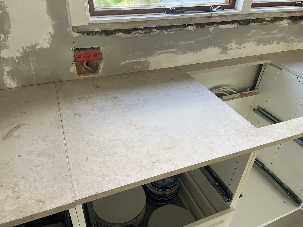 Köksbänkskiva i matt Jura Grey kalksten i Vedbæk med urtag i stenen och vit köksinredning under montering.