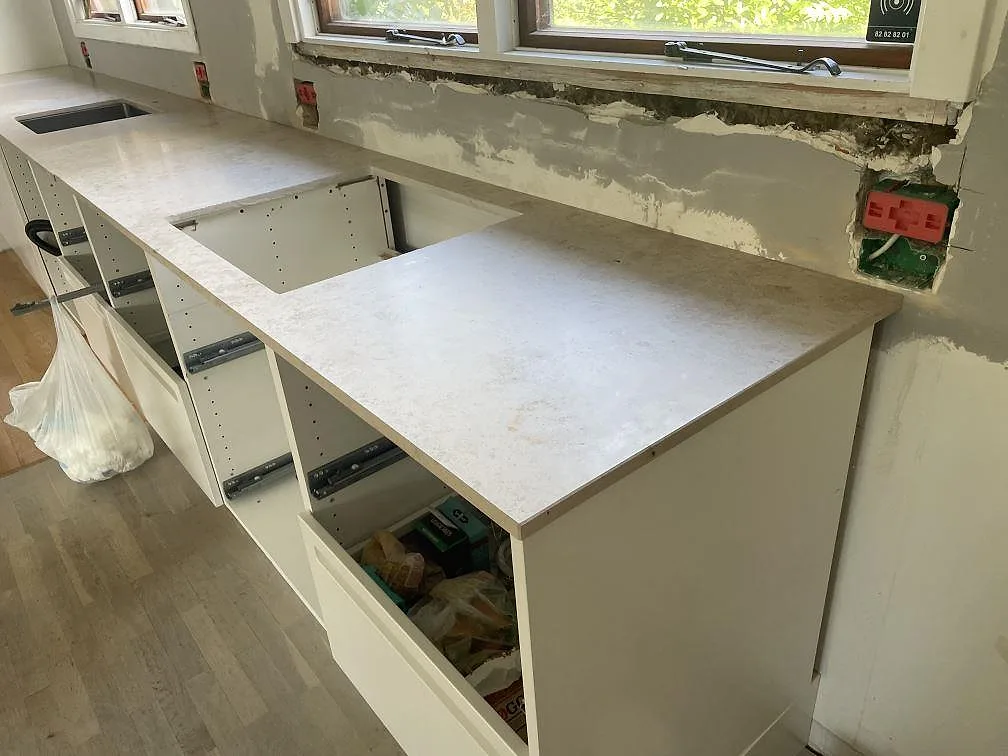 Köksbänkskiva i matt Jura Grey kalksten i Vedbæk med arbetsyta under fönster och öppna vita köksstommar.