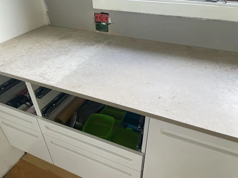 Rak detaljbild av köksbänkskiva i matt Jura Grey kalksten i Vedbæk över vita lådor och öppna stommar.