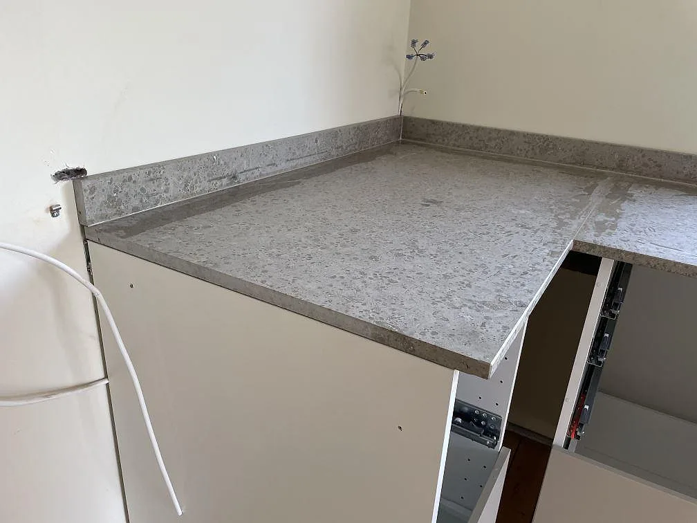 Halvö i matt Jura Grey kalksten med rak framkant och uppvikt stänkkant i ett kök under montering i Ystad.