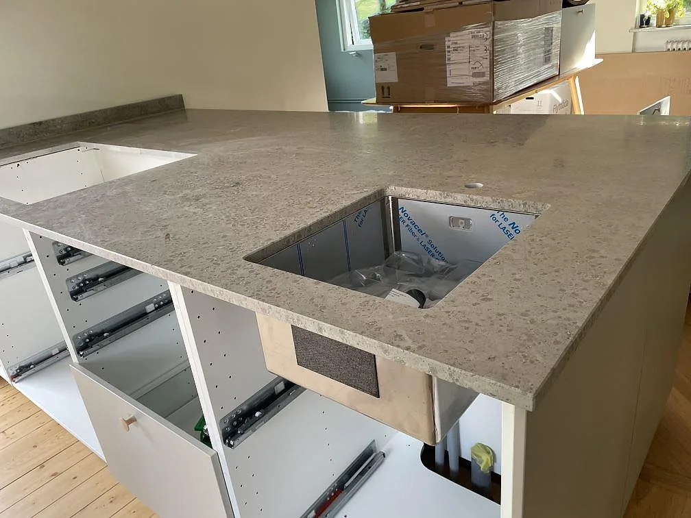 Köksbänkskiva i matt Jura Grey kalksten med underlimmad rostfri diskho och hällurtag under montering i Ystad.