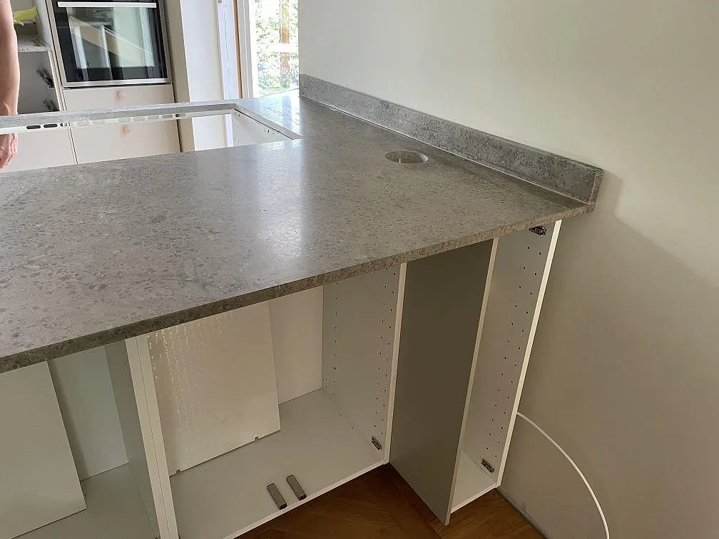 Köksbänkskiva i matt Jura Grey kalksten med urtag för häll, uppvikt stänkkant och vita stommar i Ystad.