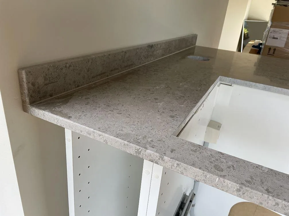 Detaljbild av matt Jura Grey kalksten med hällurtag och uppvikt stänkkant på köksbänkskiva i Ystad.