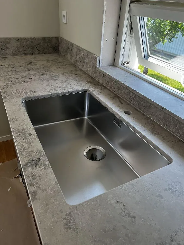 Köksbänkskiva i matt Jura Grey kalksten med underlimmad rostfri diskho vid fönster i Ytterby.