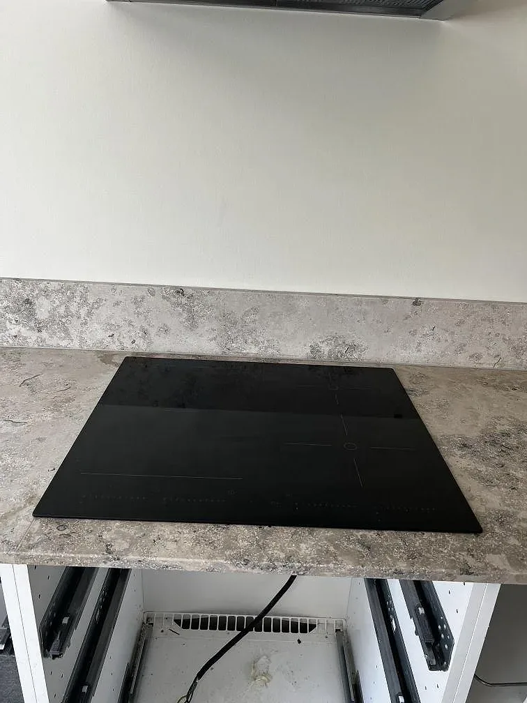 Detalj av matt Jura Grey köksbänkskiva med svart induktionshäll monterad i stenen i Ytterby.