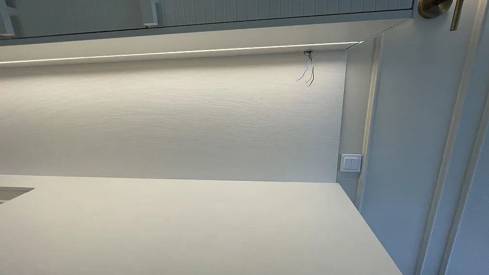 Lång väggbänk i Laminam Bianco Spacco med vit keramisk yta och belyst väggskiva i ett kök i Malmö.
