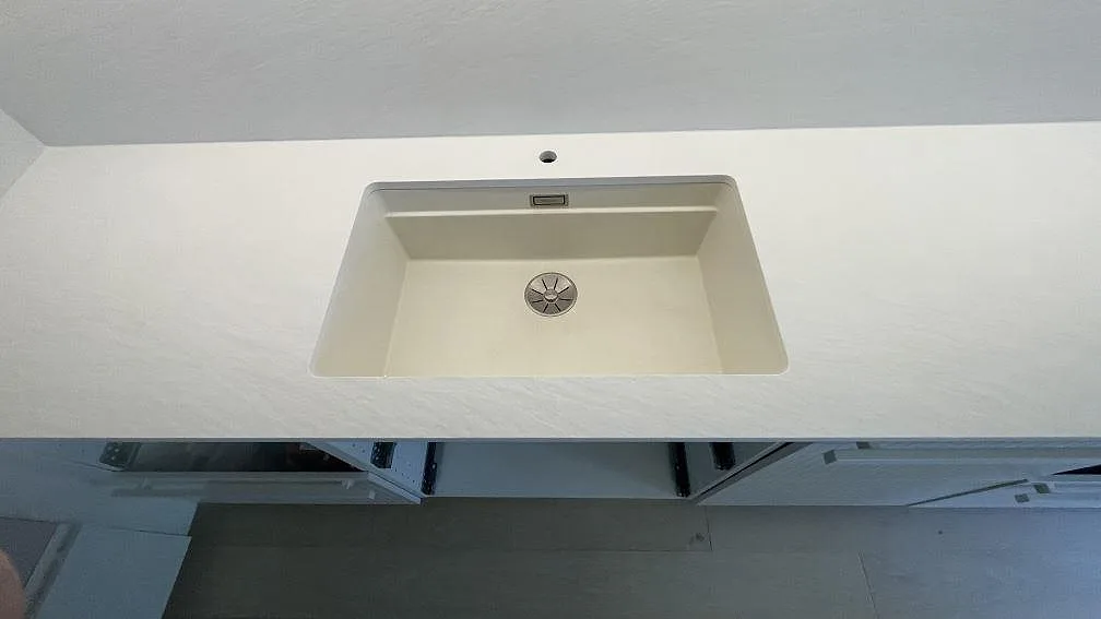 Närbild på diskhozonen i Laminam Bianco Spacco, vit strukturerad keramik, monterad över köksstommar i Malmö.