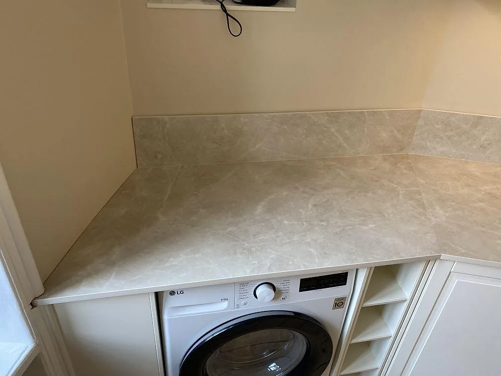 Närbild på polerad Laminam Diamond Cream bänkskiva i keramik med 12 mm stänkskydd över tvättmaskin i Malmö.