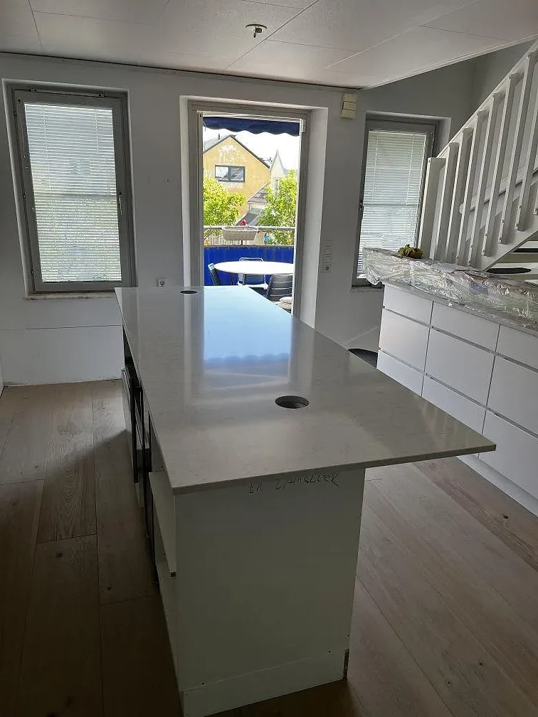Köksbänkskiva i vit Silestone Snowy Ibiza, polerad kvartskomposit, monterad som köksö med ljust ådrad yta i ett kök under montering i Limhamn.