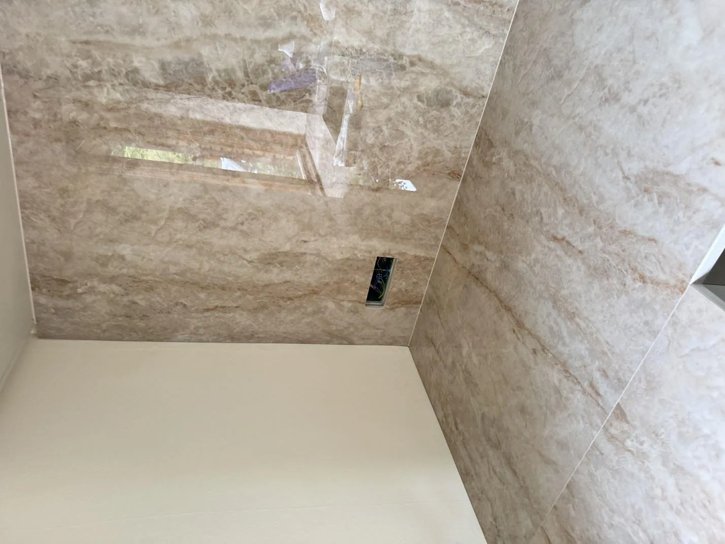 Närbild av blank Makrana väggbeklädnad med eluttag och reflektioner över köksbänken i Birkerød.