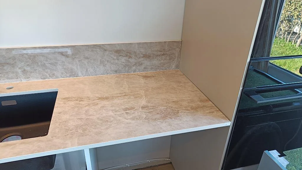 Rak köksbänkskiva i polerad Makrana keramik med mörk diskhoöppning, lågt stänkskydd och beige ådring i Helsingborg.