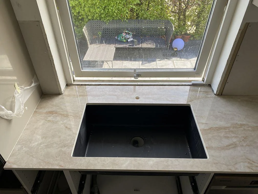 Detalj av polerad Makrana keramik vid fönstret i ett kök i Kävlinge, med blank stenreflex och monteringsskede runt bänken.