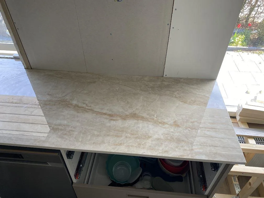 Ytnära bild av polerad Makrana köksbänkskiva i Kävlinge, med stänkkant, ljus ådring och öppna köksstommar.