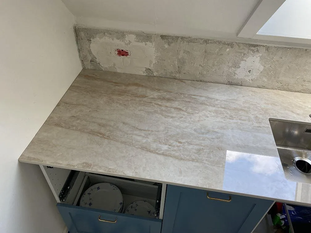 Närbild av polerad Makrana keramik på köksbänk med ljus ådring, öppna blå köksstommar och synlig diskho i København V.