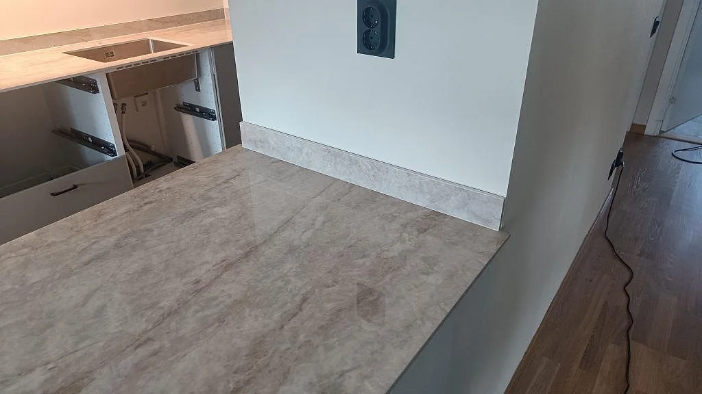Detalj av köksö i polerad Makrana keramik med låg stänkkant mot vägg och tydlig stenådring i Kungälv.