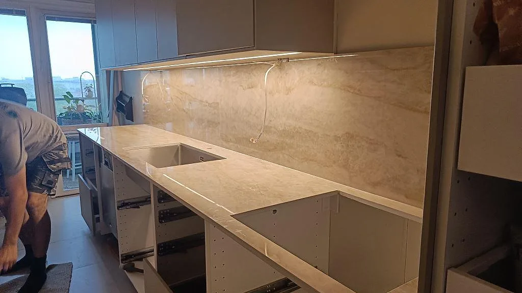 Köksbänkskiva i polerad Makrana keramik med hög väggbeklädnad och öppen montering i ett kök i Malmö.