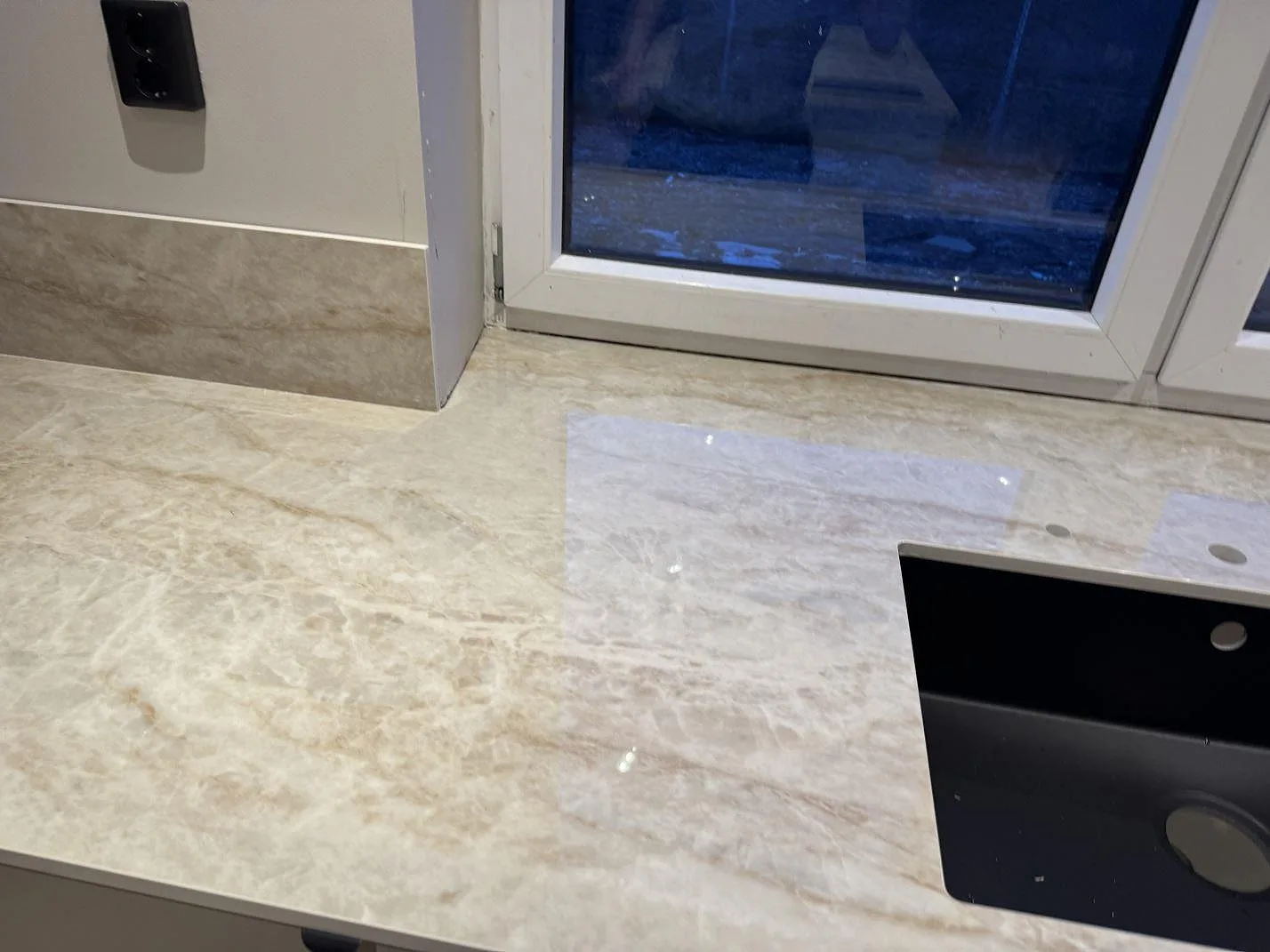 Detalj av polerad Makrana köksbänkskiva med svart diskho och hål för blandare i Malmö.