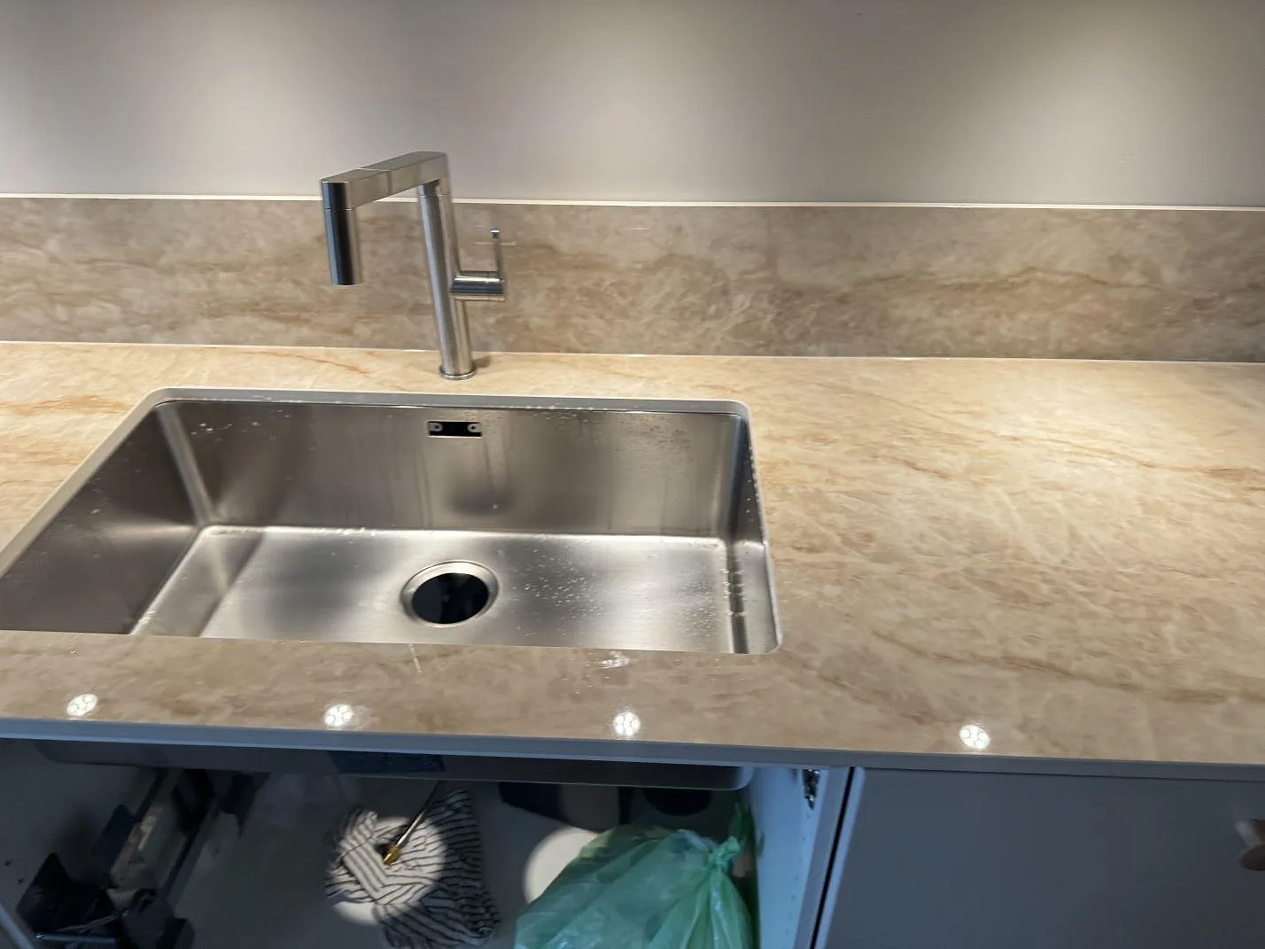 Detalj av polerad Makrana keramik runt rostfri diskho och köksblandare med matchande stänkskydd i Ödåkra.