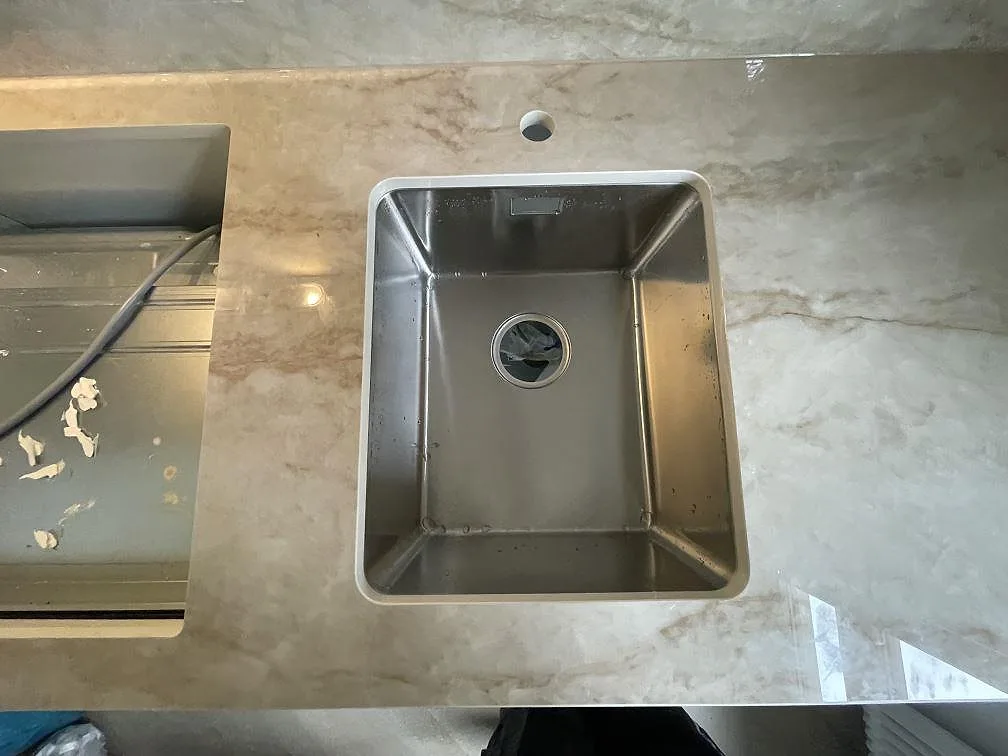 Underlimmad rostfri diskho och blandarhål i polerad beige Makrana-keramikbänkskiva i ett kök i Stockholm.