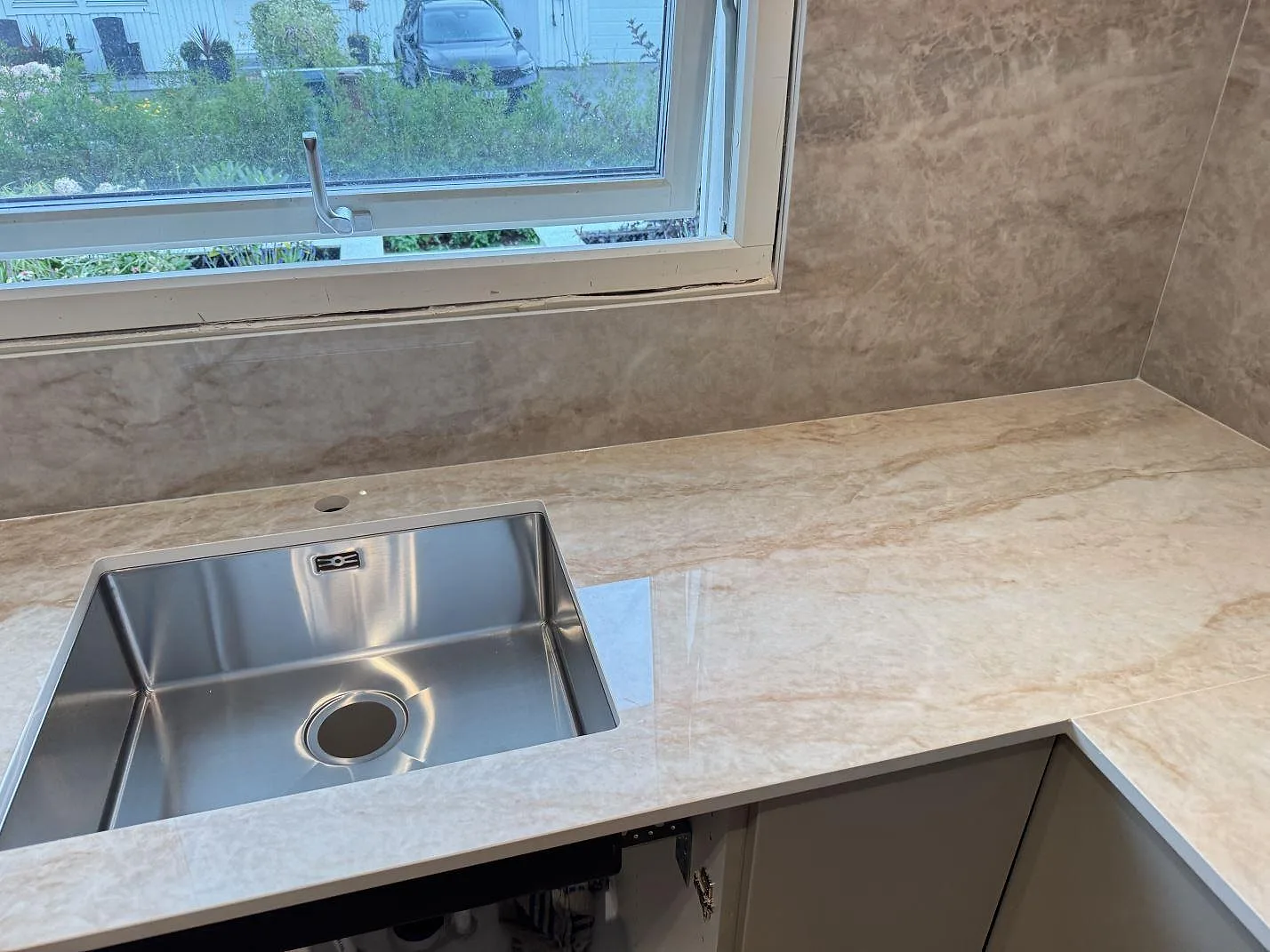 Polerad Makrana keramik runt en rostfri diskho, med matchande väggbeklädnad under fönstret i ett kök i Torslanda.