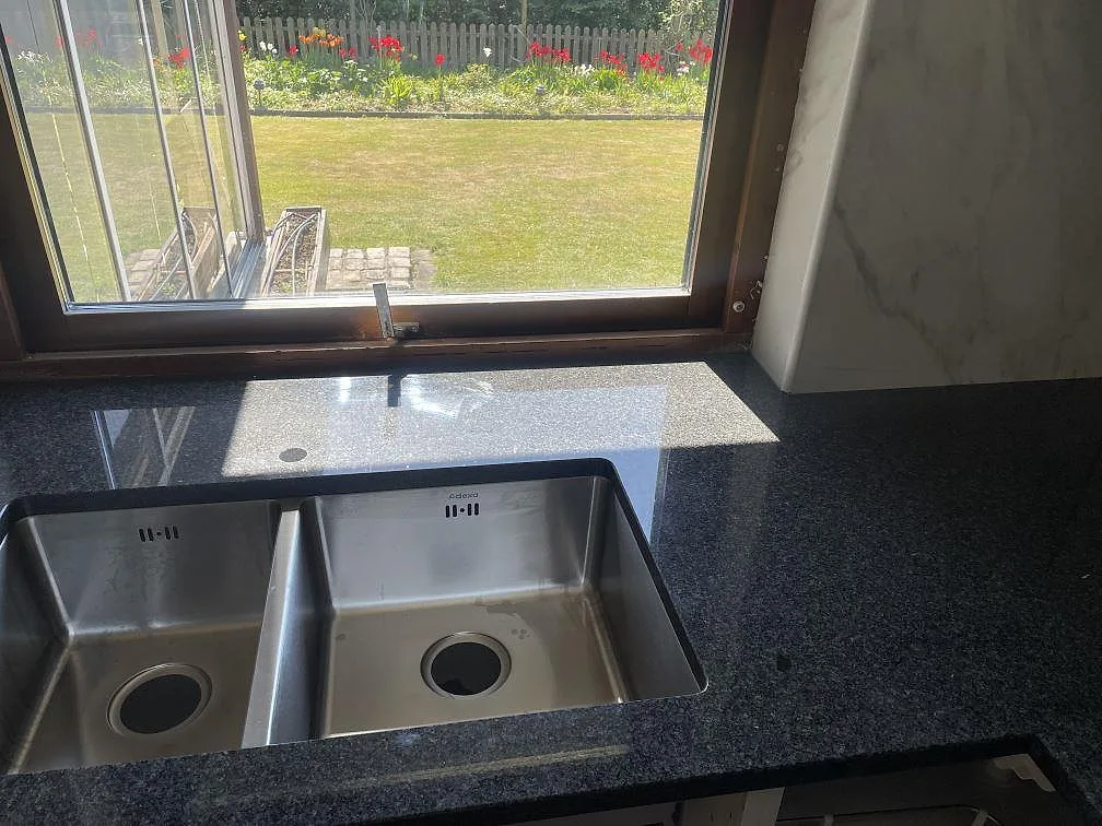 Närbild på underlimmad dubbeldiskho i rostfritt i en polerad Nero Africa granitbänkskiva i ett kök i Bjuv.