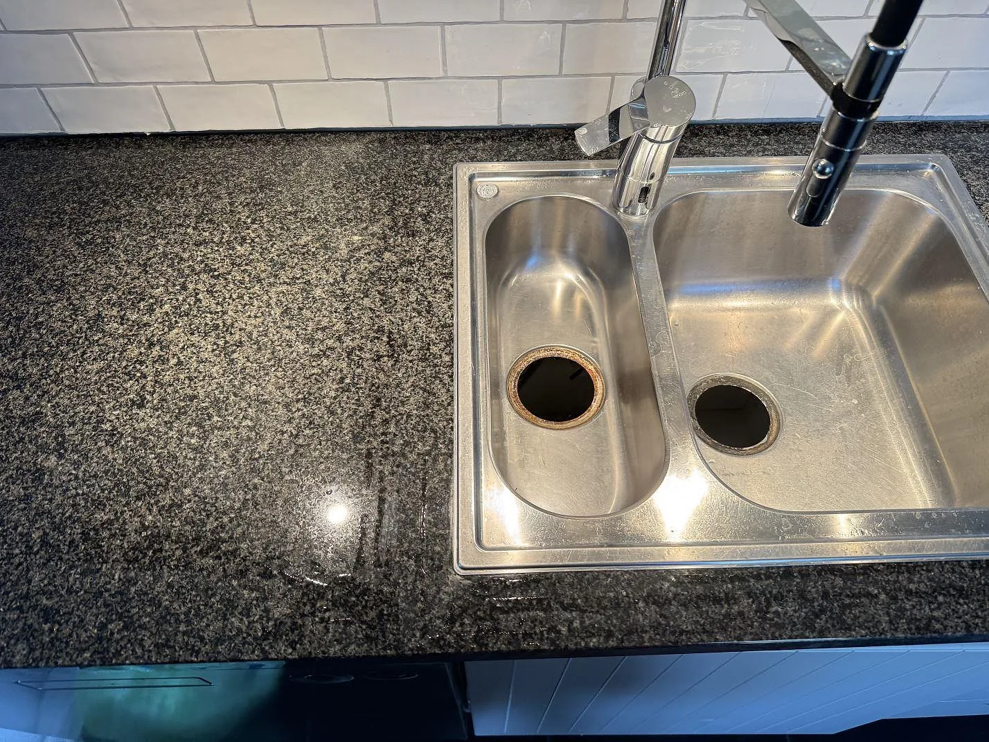 Närbild av polerad Nero Africa granit intill en rostfri dubbelho och vitt kakel i ett kök i Göteborg.