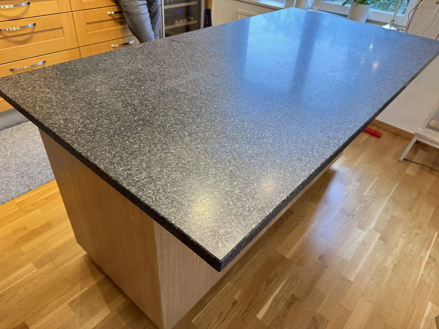 Köksö med matt Nero Africa granit, 30 mm, sedd från hörnet i ett ljust kök i Göteborg.