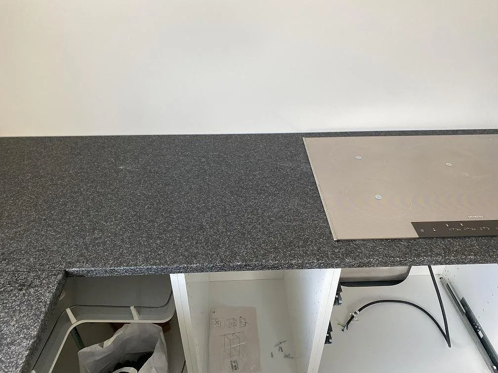 Matt Nero Africa granitbänkskiva med infälld induktionshäll längs köksvägg i Hällingsjö.