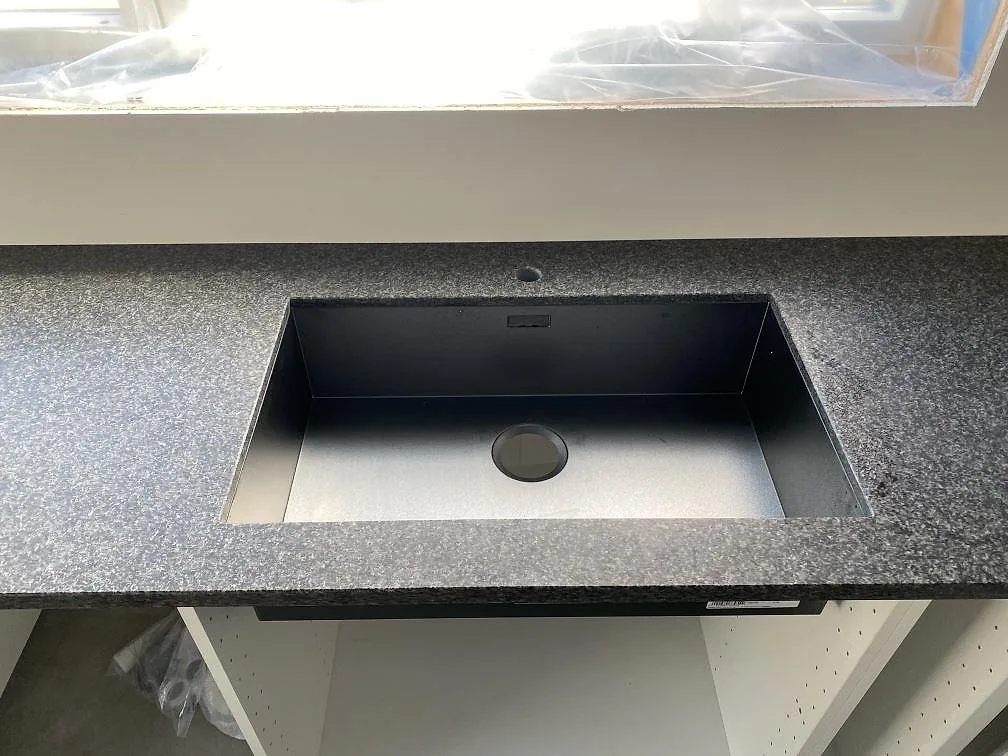 Underlimmad rostfri diskho i mörk Nero Africa granitbänkskiva vid fönster i ett kök i Hällingsjö.