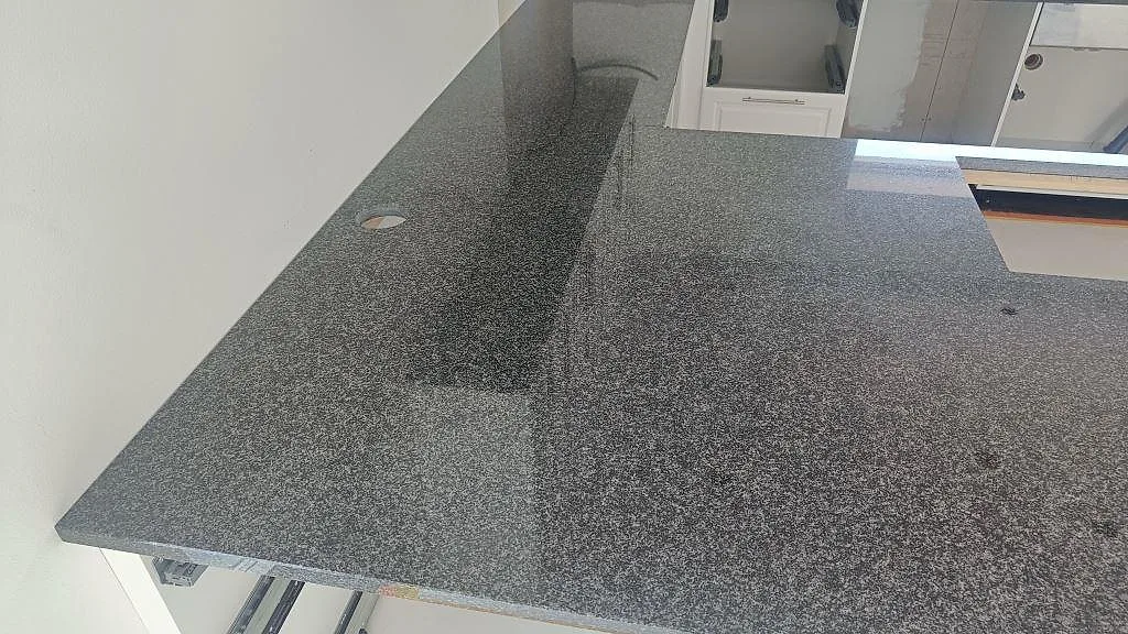 Bänkskiva i polerad Nero Africa granit längs vägg och köksö med utskärningar under montering i Halmstad.