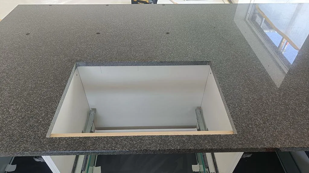 Detalj av polerad Nero Africa granit med stor öppning i köksö och speglad fönsterreflektion i Halmstad.