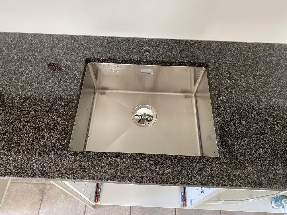 Närbild av underlimmad rostfri diskho i polerad Nero Africa granit, med blandarhål i köket i Hjärnarp.
