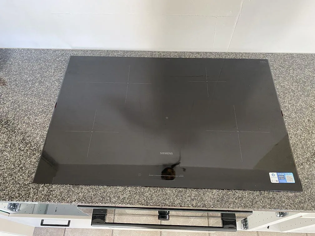 Induktionshäll monterad i polerad Nero Africa granit, med gråsvart köksbänkskiva under montering i Hjärnarp.