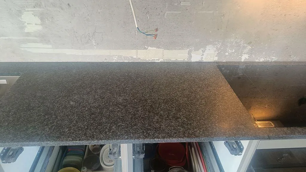 Lång bänkyta i matt Nero Africa granit med hällzon och öppna köksstommar under montering i Lomma.