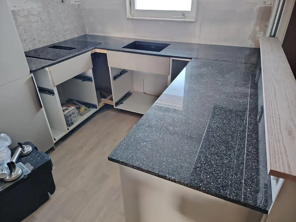 Köksbänkskiva i polerad Nero Africa granit, 20 mm, monterad i ett L-format kök i Nacka med synliga öppningar för diskho och häll.