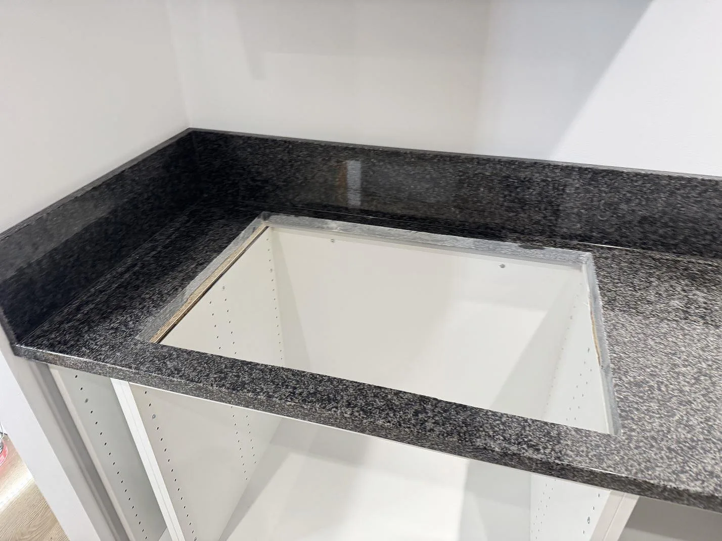 Närbild av installerad Nero Africa granit i polerad yta runt en öppen köksstomme och stänkskydd i Rydsgård.