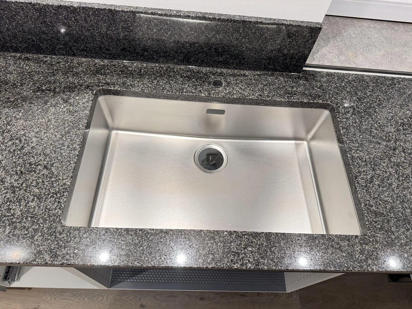 Detalj av polerad Nero Africa granit runt en underlimmad rostfri diskho och blandarhål i ett kök i Rydsgård.