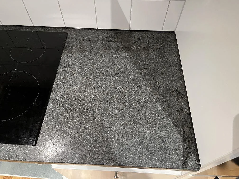 Köksbänkskiva i polerad Nero Africa-granit med infälld induktionshäll och vit kakelvägg i Skärhamn.