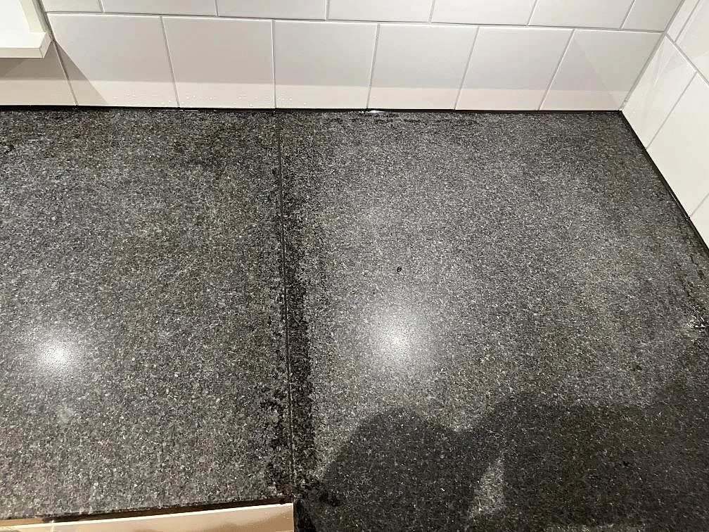Ovanifrån av polerad Nero Africa-granit som köksbänkskiva med synlig skarv mot vitt kakel i Skärhamn.