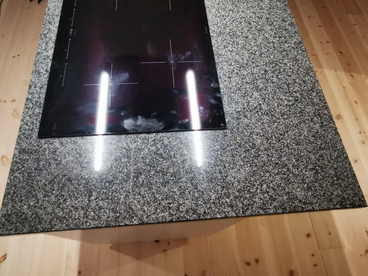 Närbild på köksö i Nero Africa granit, polerad svart sten med induktionshäll infälld ovanpå, i ett kök i Vaggeryd.