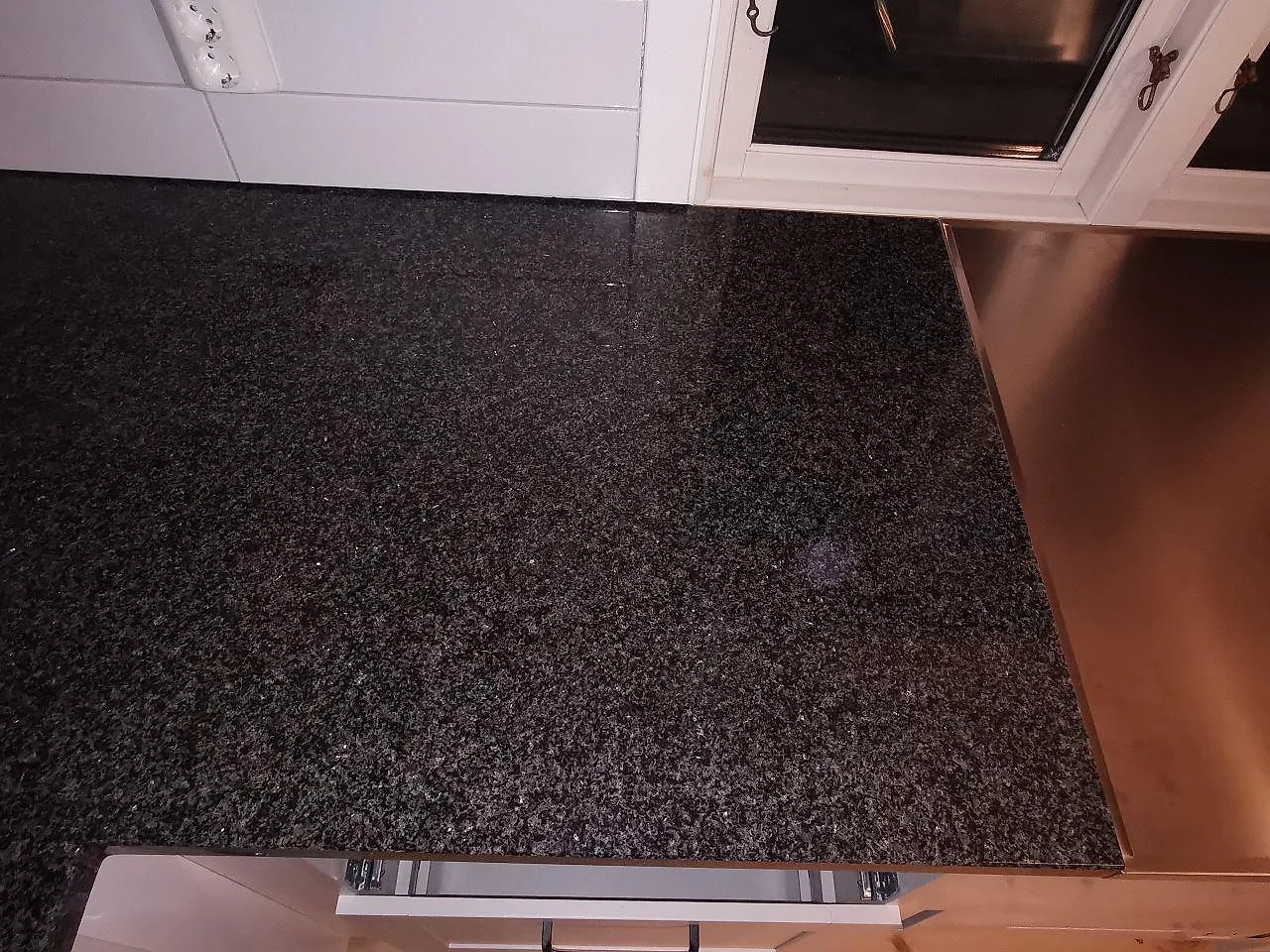 Bänkskiva i polerad Nero Africa granit längs köksväggen, mörk granityta med synlig kristallstruktur, i ett kök i Vaggeryd.