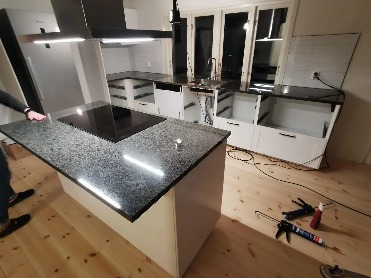 Köksbänkskiva och köksö i mörk Nero Africa granit, polerad, med övermonterad induktionshäll i ett kök under montering i Vaggeryd.