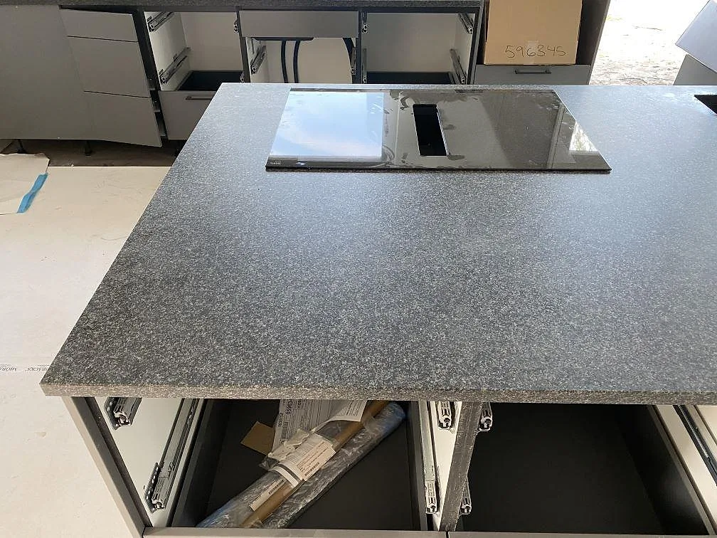 Köksö med matt Nero Africa granit, infälld häll och öppna köksstommar under montering i Vilshärad.