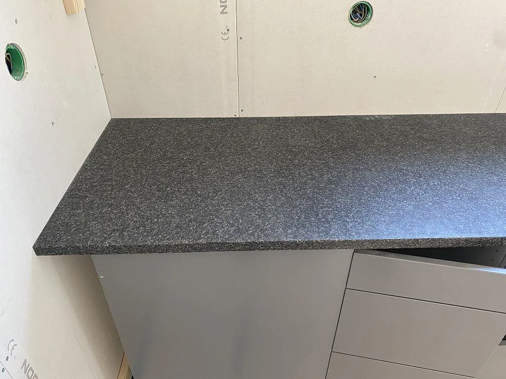 Sidovy av väggbänk i matt Nero Africa granit över ljusa skåpstommar i Vilshärad.
